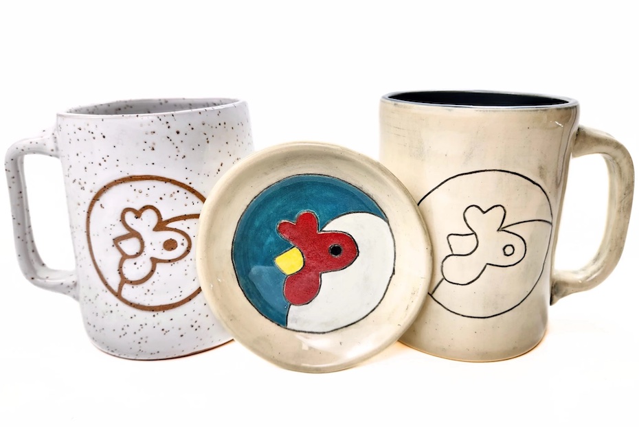 Two handmade pottery mugs made from stoneware. One mug is white speckled and the other is an off-white with a black line glaze. The dish is full color painted glaze. All feature the Artisans Cooperative logo chicken mascot